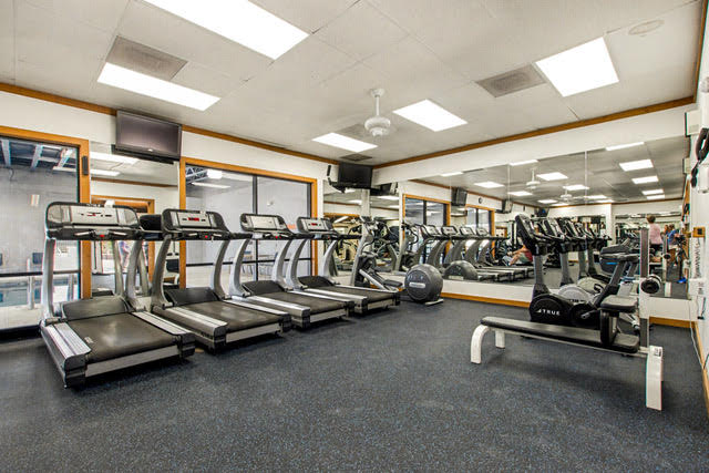 A gym with several treadmills, exercise bikes, and other cardio equipment, with large mirrors covering the walls.